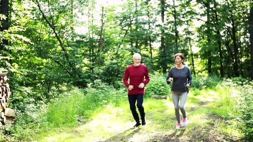 Senior Sporty Couple Running In The Forest Outdoors In Sunny Nature.