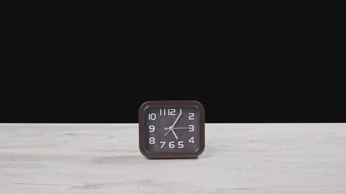 El reloj puntero sobre mesa de madera y fondo negro muestra la hora