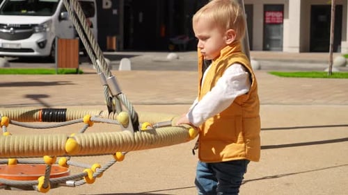 Little baby boy playing outdoor on the playground with nest rope swing