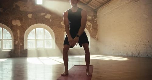 A Young Man in a Black Sports Uniform in the Sunny Hall is Engaged in Fitness on a Special Rug