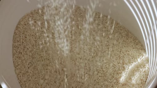 top view of person grabbing many raw grains of rice and falling into bucket,close up