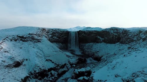 Winter landscape with a waterfall plunging over a cliff at dusk - push in drone