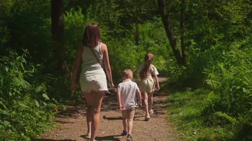 Mother and Couple of Children Walk Along Path in Green Park