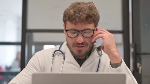Close Up of Doctor Talking on Phone while Working on Laptop
