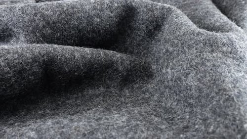 Close-up view of the soft folds of textured gray wool fabric rotated on the display case.