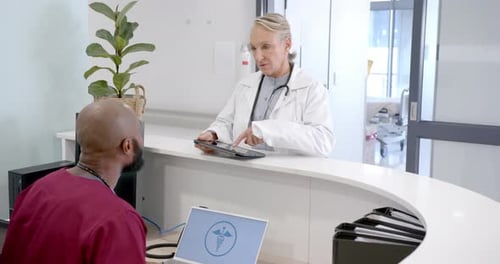 Diverse male and female doctors in discussion using tablet in hospital reception, slow motion