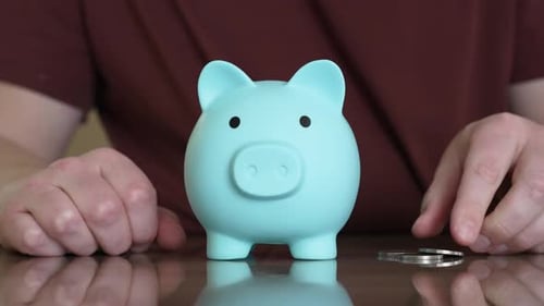 Person inserting coins into a light blue piggy bank