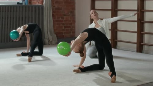 Two Graceful Girls Practicing Exercise with Balls on the Floor in Gym