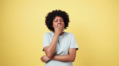 Jeune femme endormie bâillant et s'étirant sur fond jaune