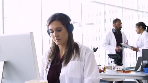 Dedicated female scientist in headphones working at computer in science laboratory
