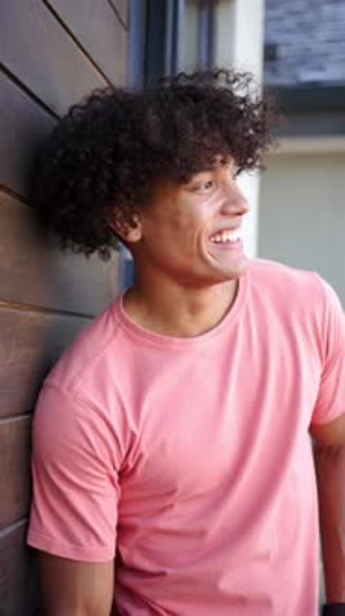Vidéo verticale : Un jeune homme biracial au sourire éclatant s'appuie contre un mur en bois