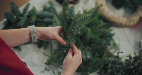 Woman Arranges Christmas Wreath on a Table