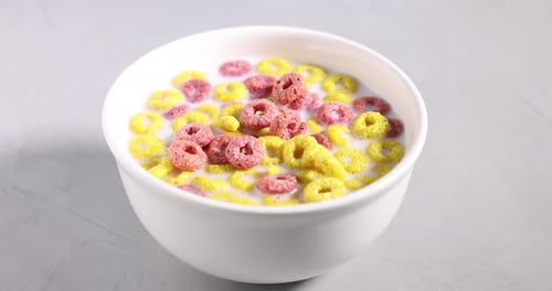 Breakfast cereal falling into bowl with milk on light table, closeup