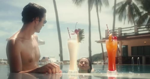 Poolside with happy couple enjoying holidays with drinks at resort swimming pool