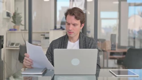 Man Frustrated with Documents and Laptop at Desk