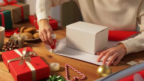 Woman Wrapping Christmas Gift on Table with Decorations
