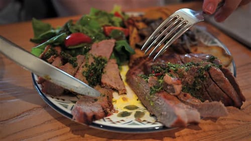 Person cutting grilled meat served with salad and roasted potatoes on plate