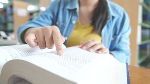 Student doing research in library using laptop in books making a project and preparing for exam.