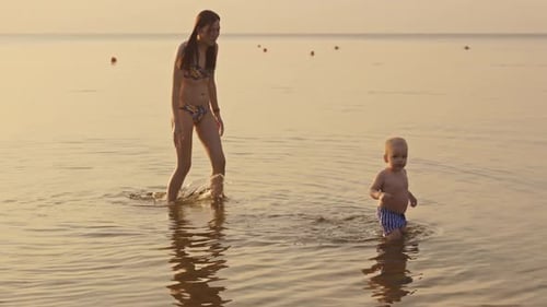 A Peaceful Beach Day A Mother and Her Child Relishing the Joy of the Waves While Watching the Sunset