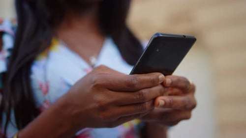 African american woman typing message on mobile phone in urban city street