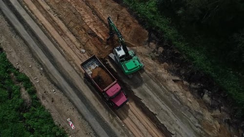 Top-down aerial view of truck and bulldozer loading and unloading soil at the road construction site