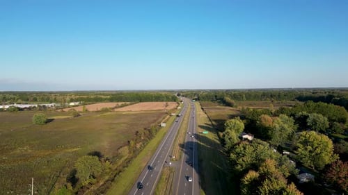 An aerial view capturing a highway cutting through expansive open fields on a clear day. Ideal for s