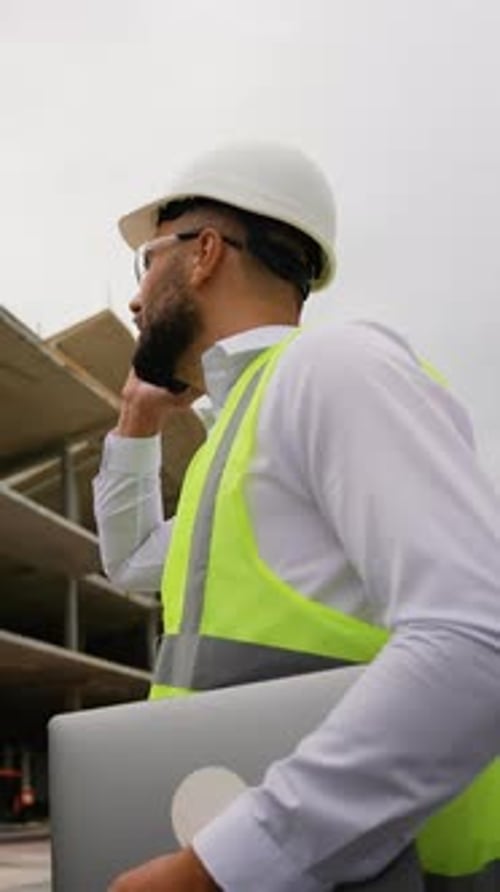 Civil Engineer with Laptop Talking on Smartphone at Construction Site