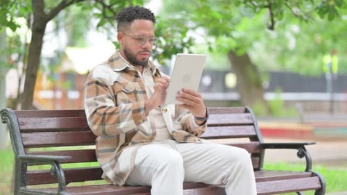 Hispanischer Mann benutzt ein digitales Tablet, während er im Freien sitzt