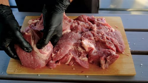 Gloved Hands Preparing and Salting Meat on Cutting Board