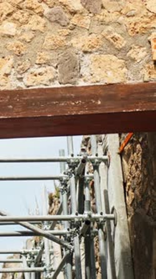 Vertical close-up of metal scaffolding and wooden bracing supporting ancient Pompeii masonry, with