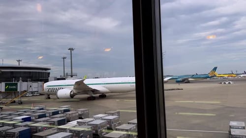 Ein Verkehrsflugzeug ist an einem belebten Flughafenterminal unter bewölktem Himmel geparkt
