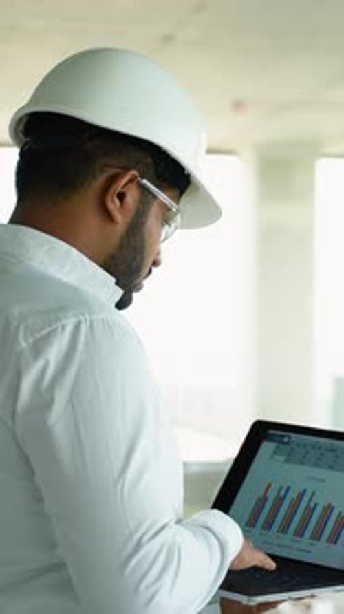 Man in Hardhat with Laptop at Construction Site
