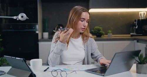 Focused young caucasian woman with long hair sit at desk at home office work on laptop record audio