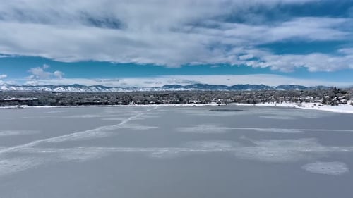 Rising aerial of Denver's Sloan Lake frozen over revealing residential housing covered in snow.