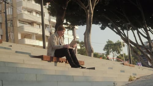 Young Adult Works on Laptop Outdoors in City