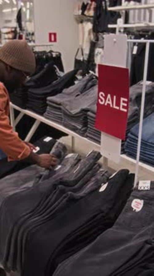 Vertical of Black Man Choosing Right Size of Jeans in Sales Section in Shop