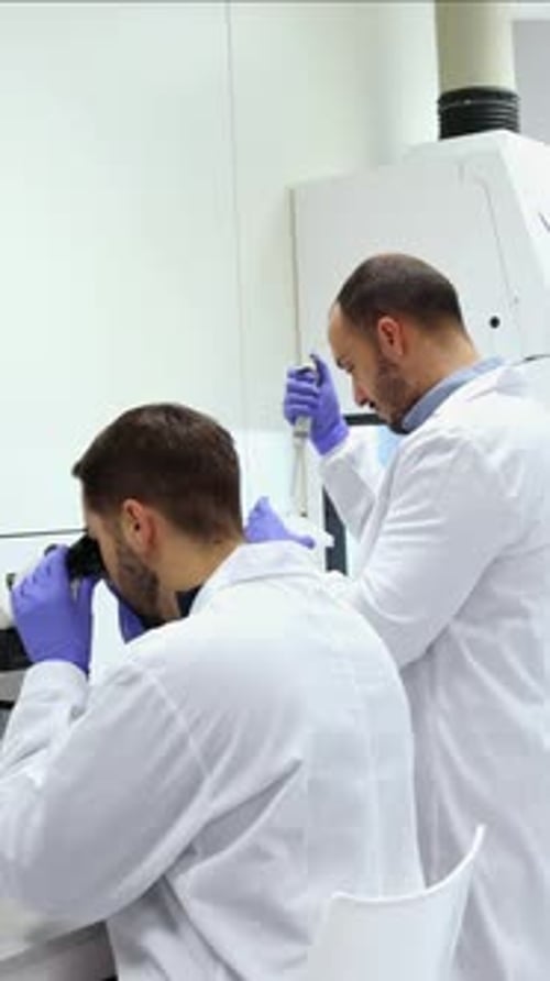 vertical Scientists working in laboratory using microscope and pipette