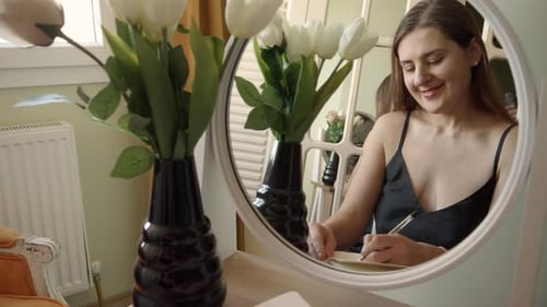 Woman Writing in Journal at Vanity Mirror