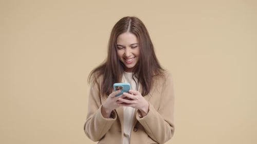 Cheerful woman using mobile phone against plain backdrop