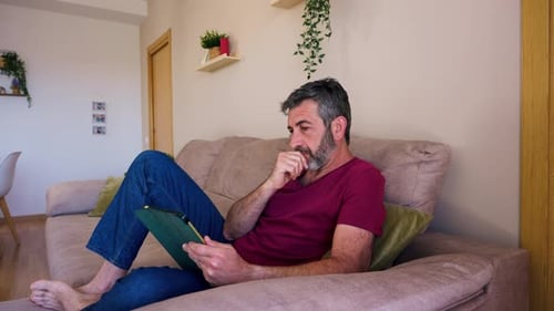 Man Relaxes on Couch Reading Tablet Device