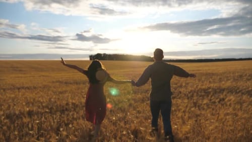 Young Couple Holding Hands of Each Other and Running Through the Wheat Field at Sunset Man and Woman