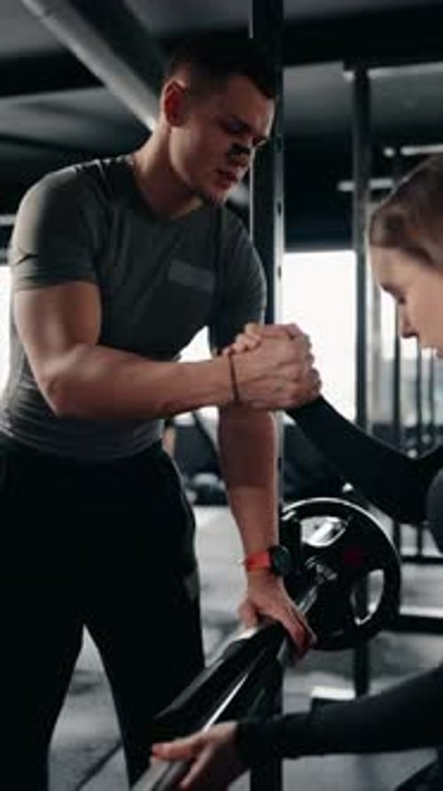 Fitness Trainer Supports and Motivates Woman During Weightlifting in Gym