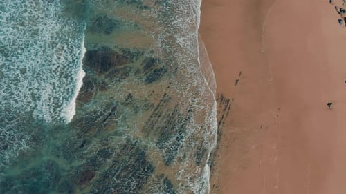 Breathtaking top-down aerial view of beach and reef. The sea is making waves for surfers.