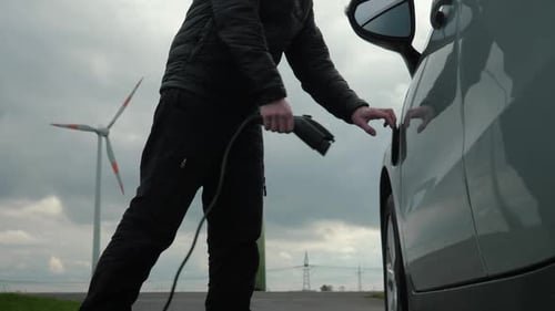 Man Charges Electric Car near Wind Turbines