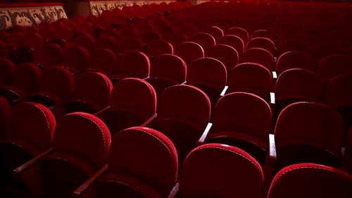 Rows of empty red velvet seats inside a theater or opera. No people in hall because of pandemic.