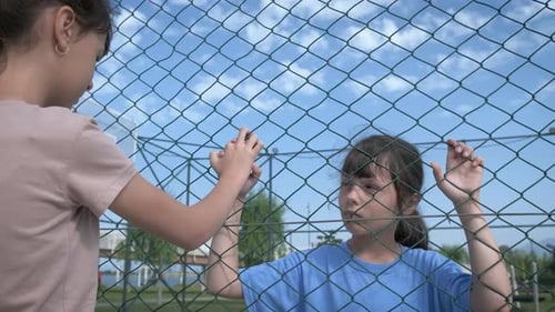 Two Children Holding Hands Through a Chainlink Fence