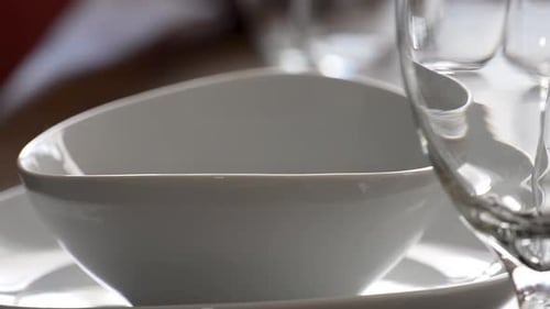 Setting Dinner Table with Empty Wine Glasses and an Empty White Soup Bowl Close Up with Panning Moti