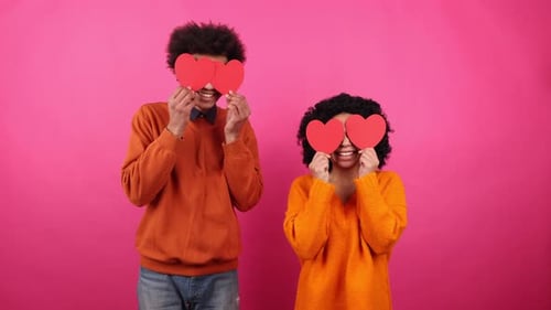 Couple Hiding Behind Valentine Hearts on Pink