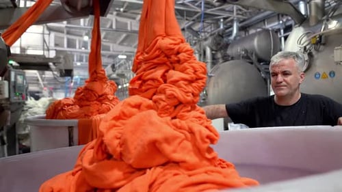 Textile Factory Worker Watching Orange Fabric Being Processed