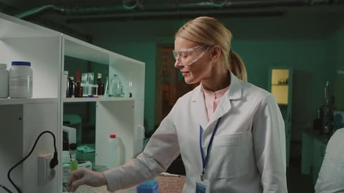 Footage of Attractive Caucasian Woman in White Lab Coat and Protective Glasses Holding Test Tube in